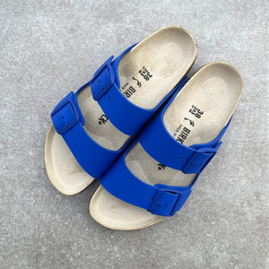 Blue Birkenstock sandals with blue soles on a grey surface