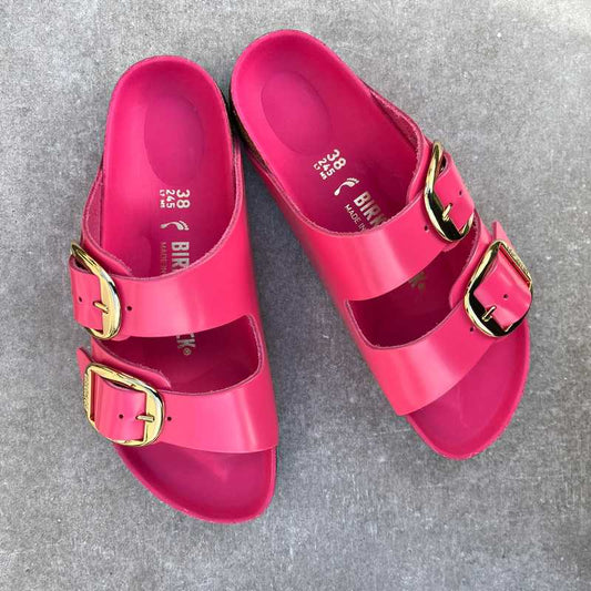 Pair of pink Birkenstock sandals with big gold buckles on a gray background