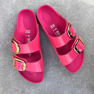 Pair of pink Birkenstock sandals with big gold buckles on a gray background