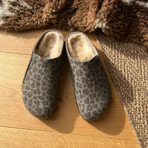 Pair of leopard print slippers with shearling lining on a wooden floor with a textured rug.