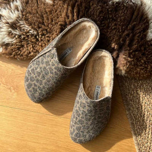 Pair of brown Animal print slippers with wool lining on a wooden floor with a textured rug in the background