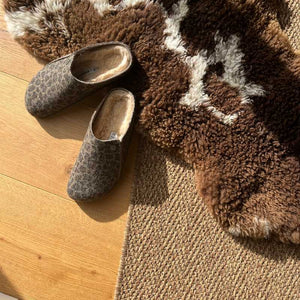 Pair of Birkenstock brown animal print slippers on a wooden floor with a textured rug.