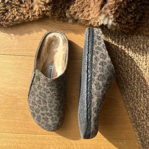 Pair of brown Birkenstock slippers on a wooden floor with a textured brown rug.