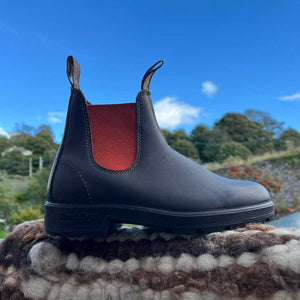 Brown Blundstone boot with Orange lining. Australian work boots on a textured surface against a blue sky with clouds.