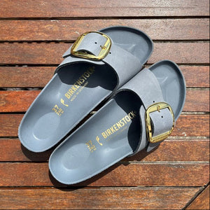 Gray Birkenstock sandals with gold buckles on a wooden surface